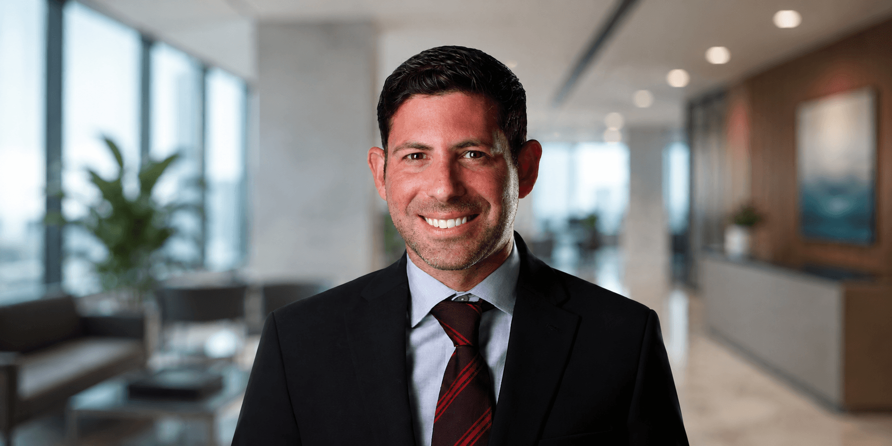 A smiling man in a suit stands in a modern office setting