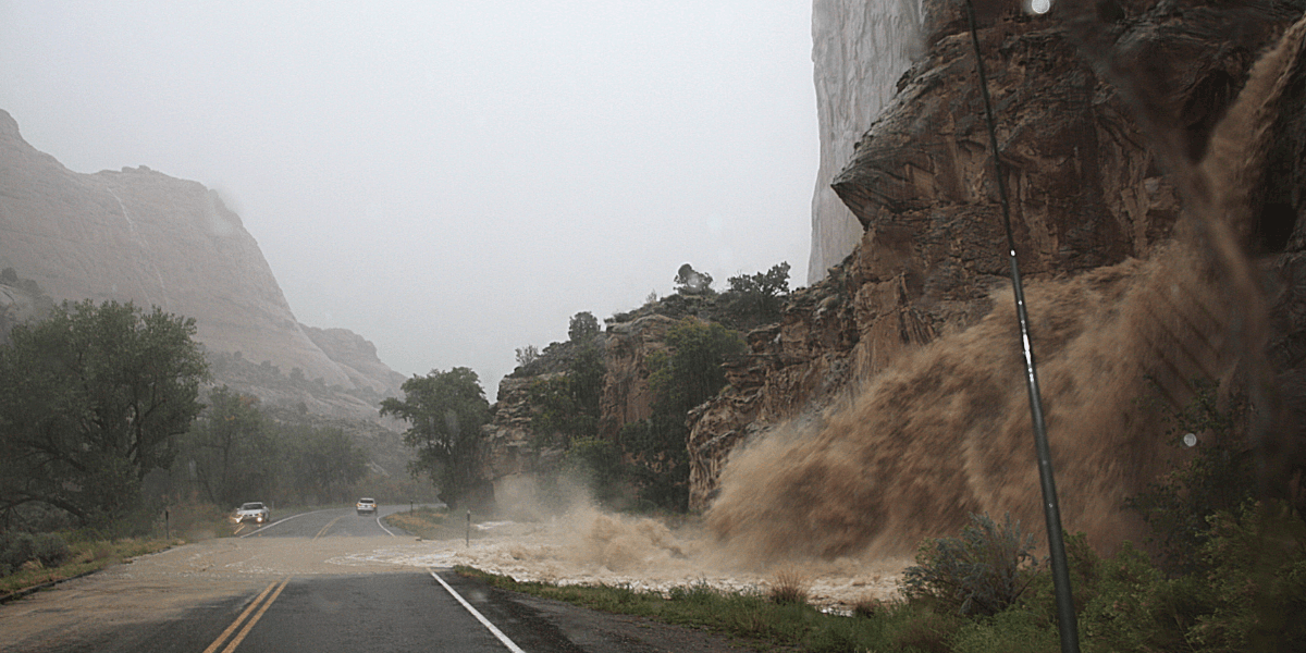 Mudslide cascading from a cliff onto a rain-soaked road during a storm