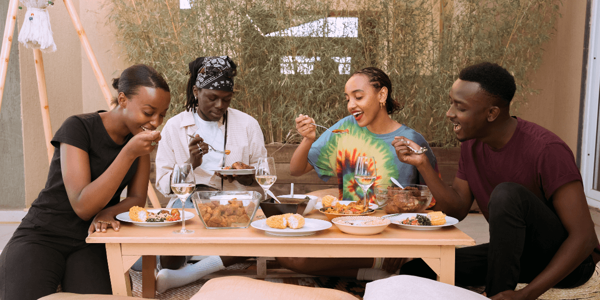 Four people enjoying a meal together at a table outdoors, smiling and sharing food