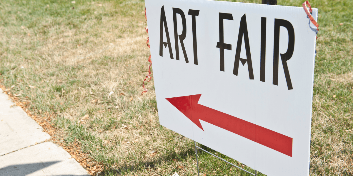 Directional sign for an art fair with an arrow pointing left on grass