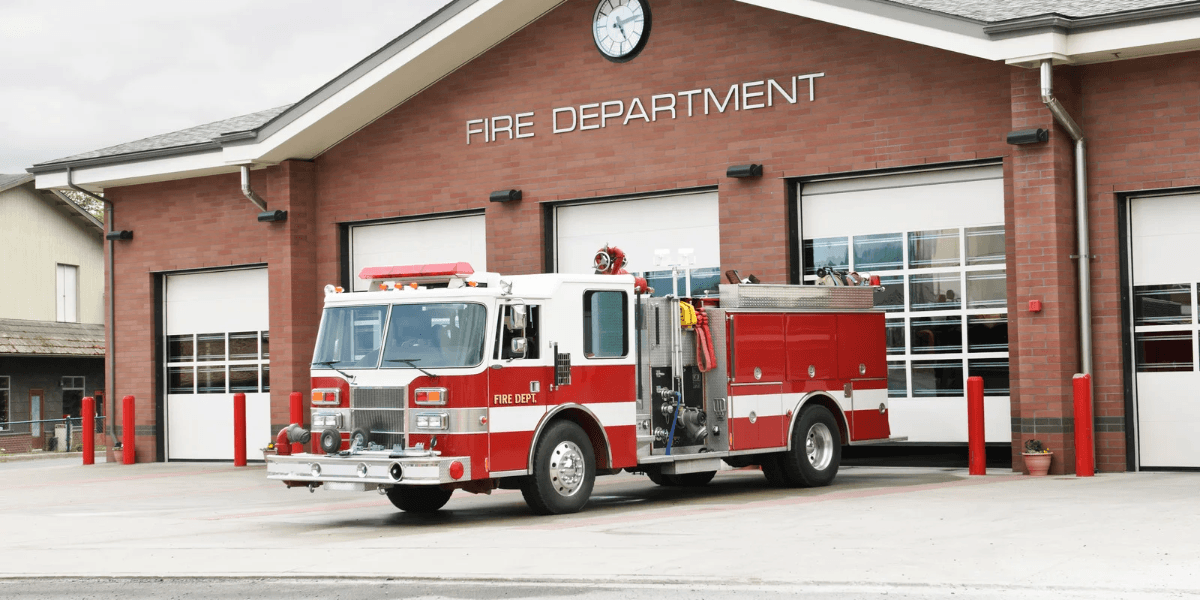 A fire truck parked in front of a fire department building with closed garage doors