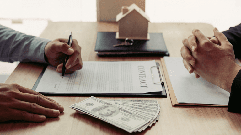 Person signs a home purchase contract with cash and a model house on the table.