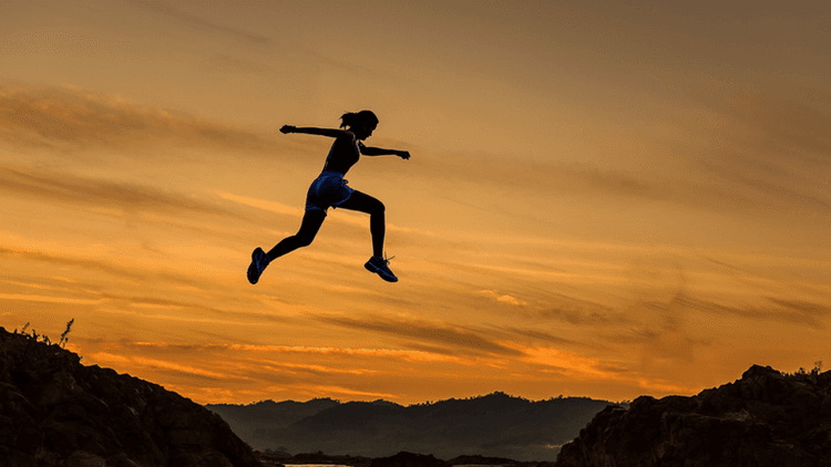Silhouette of a runner leaping between rocky cliffs at sunset.