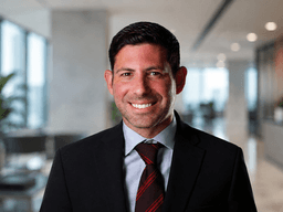 A smiling man in a suit stands in a modern office setting