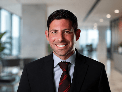 A smiling man in a suit stands in a modern office setting
