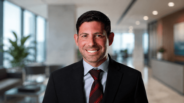 A smiling man in a suit stands in a modern office setting