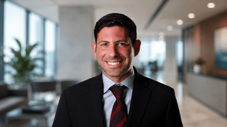 A smiling man in a suit stands in a modern office setting