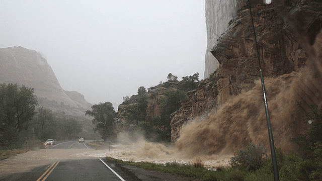 Mudslide cascading from a cliff onto a rain-soaked road during a storm