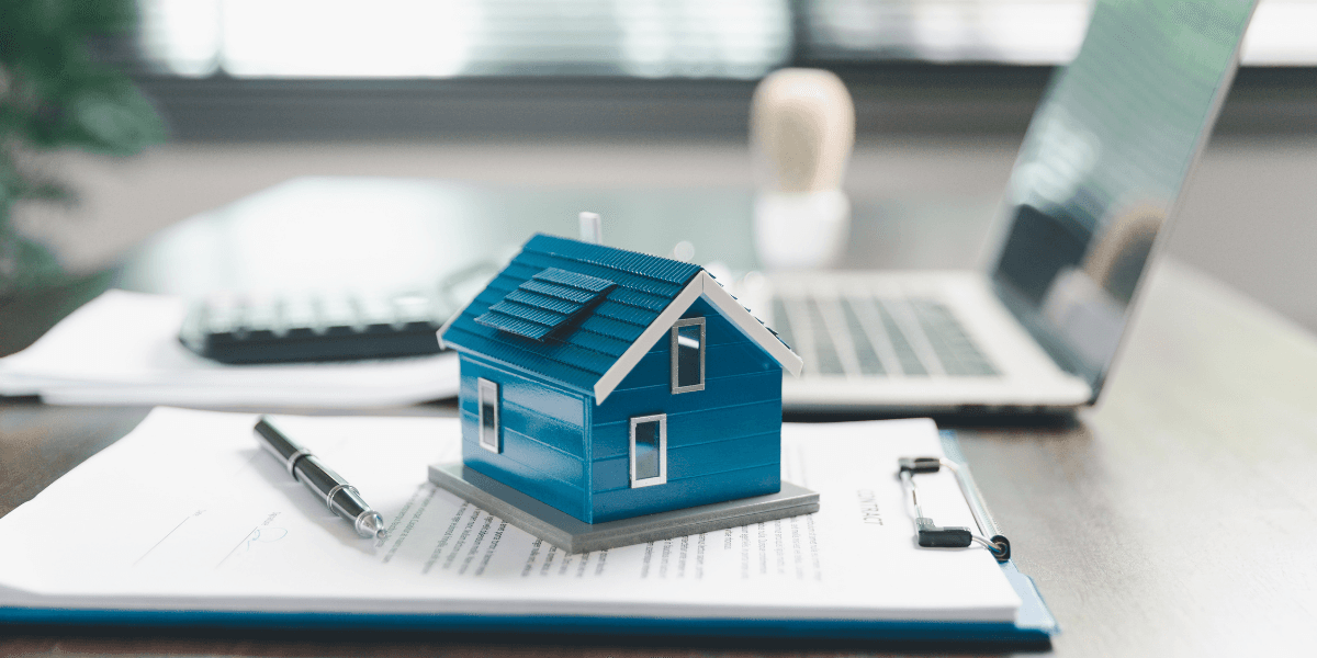 A blue model house on paperwork with a laptop and calculator in the background