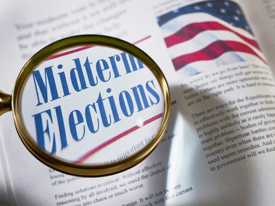 Magnifying glass over a page featuring the words "Midterm Elections" and an American flag