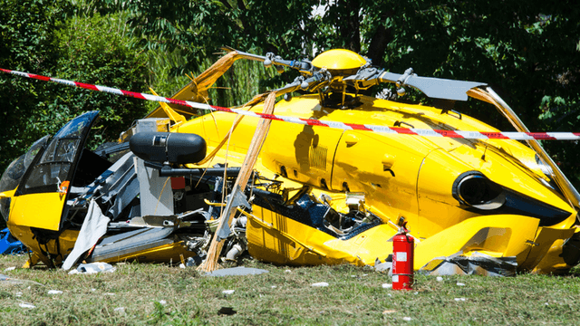 Wreckage of a yellow helicopter lying on the ground with fire extinguisher nearby