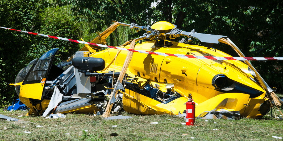 Wreckage of a yellow helicopter lying on the ground with fire extinguisher nearby