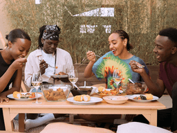 Four people enjoying a meal together at a table outdoors, smiling and sharing food