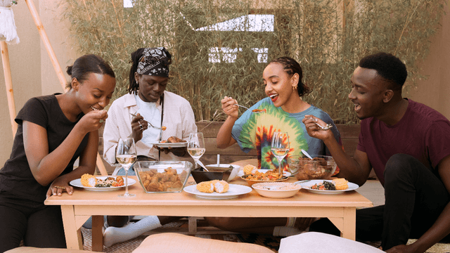 Four people enjoying a meal together at a table outdoors, smiling and sharing food