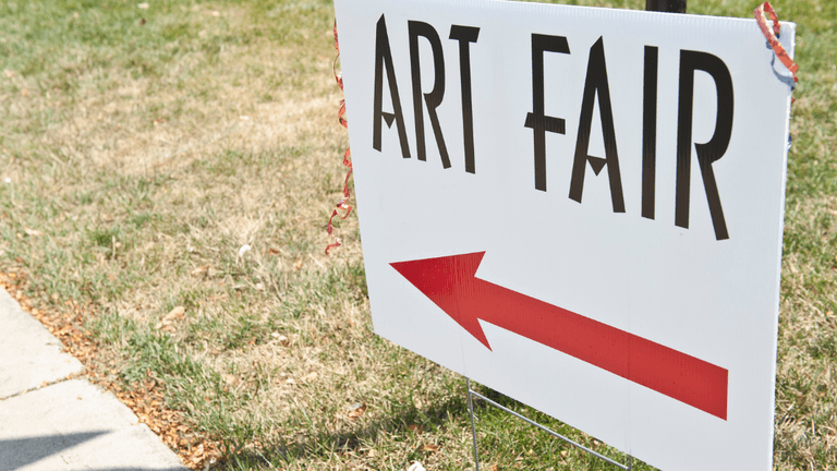 Directional sign for an art fair with an arrow pointing left on grass