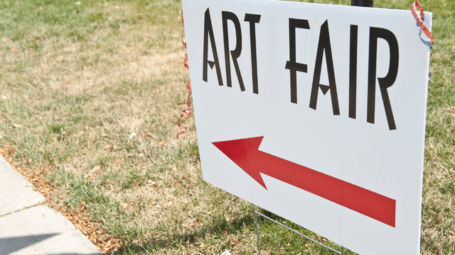Directional sign for an art fair with an arrow pointing left on grass