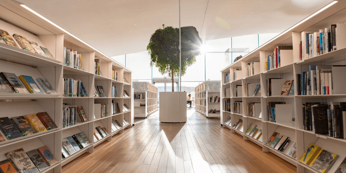 Sunlit library interior with rows of bookshelves and a central plant display