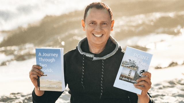 Man holding two books outdoors, smiling against a beach background.