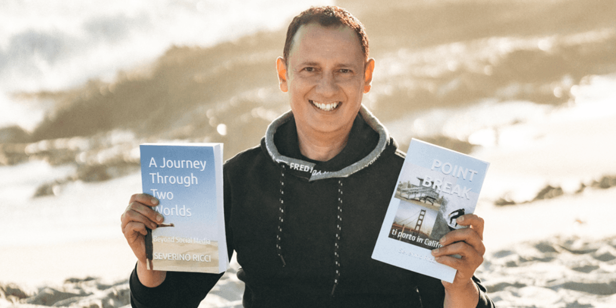 Man holding two books outdoors, smiling against a beach background.