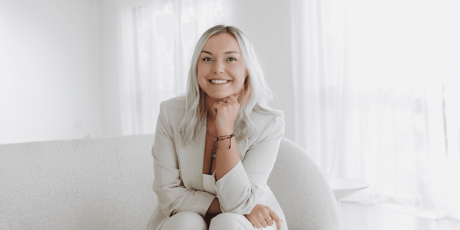 Smiling woman in a light suit seated on a couch in a bright room