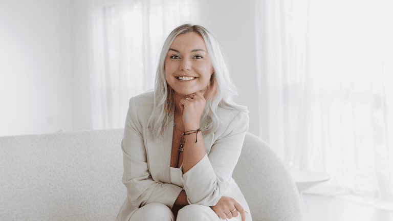 Smiling woman in a light suit seated on a couch in a bright room