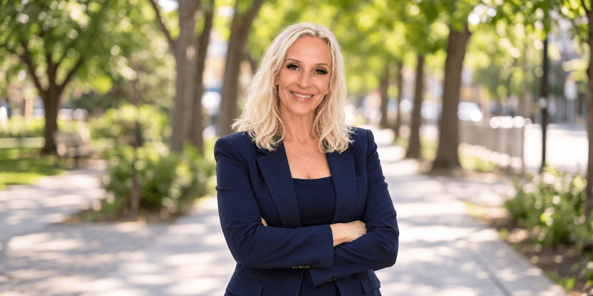 Smiling woman in a navy suit stands confidently on a tree-lined pathway