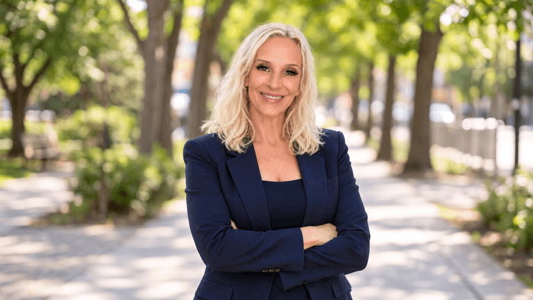 Smiling woman in a navy suit stands confidently on a tree-lined pathway