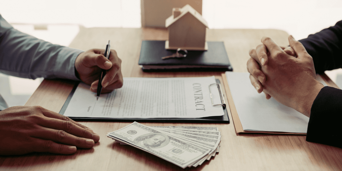Person signs a home purchase contract with cash and a model house on the table.