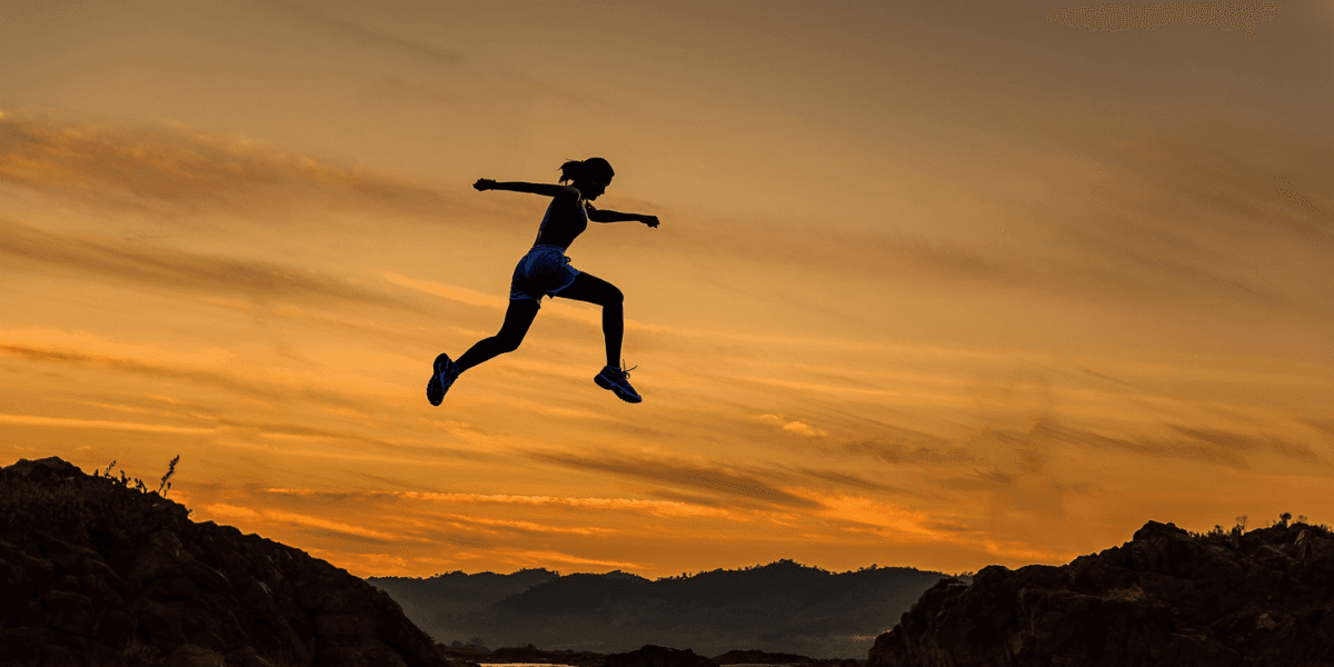 Silhouette of a runner leaping between rocky cliffs at sunset.