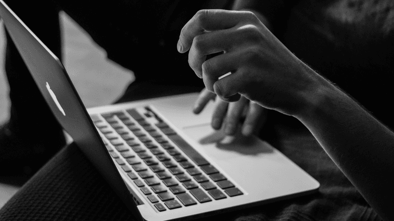 Close-up of a person's hand typing on a MacBook keyboard in black and white.