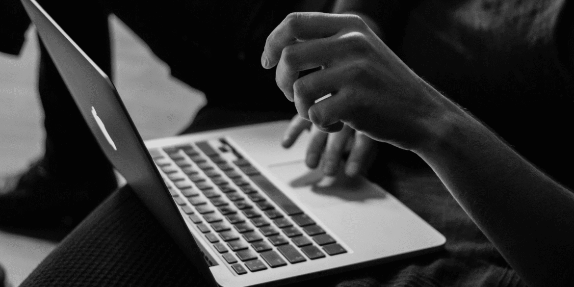 Close-up of a person's hand typing on a MacBook keyboard in black and white.