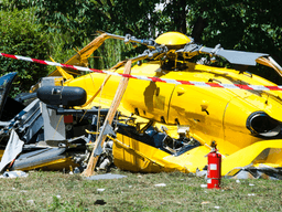 Wreckage of a yellow helicopter lying on the ground with fire extinguisher nearby